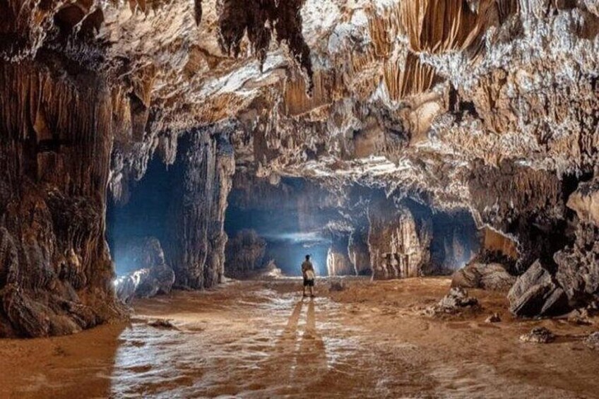 A cave with stalactites and stalagmites, a person standing in the middle, and a water body at the cave's entrance. 3