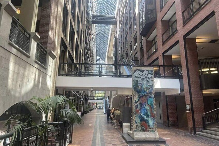 Un pasillo interior con un camino central, plantas en macetas y una gran escultura abstracta. 2