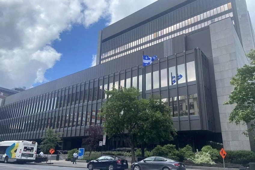 Un edificio moderno con fachada de vidrio, una bandera azul y una calle con coches y un autobús. 4