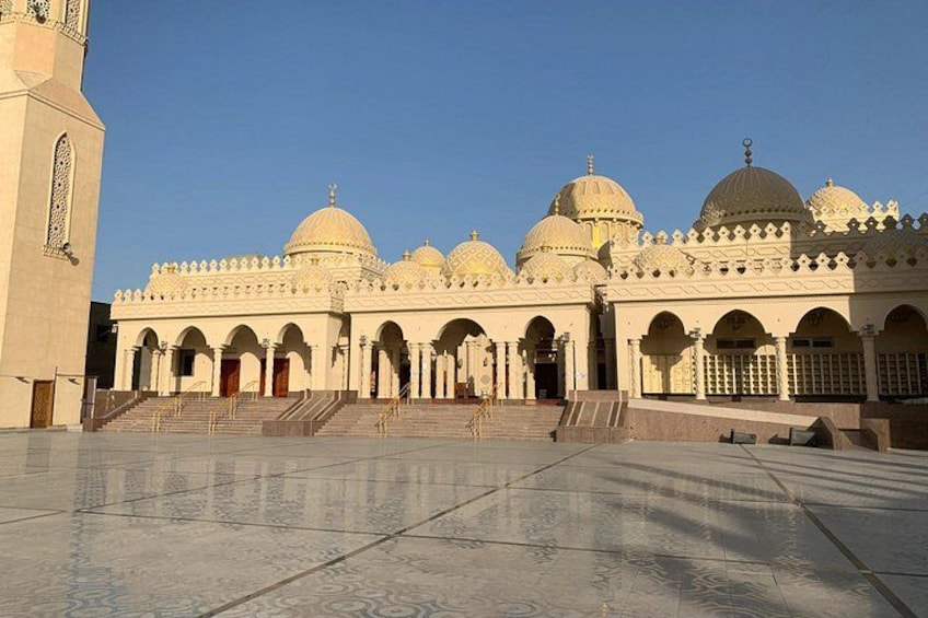 Un edificio grande y blanco con múltiples cúpulas, un patio central y un minarete alto. 4