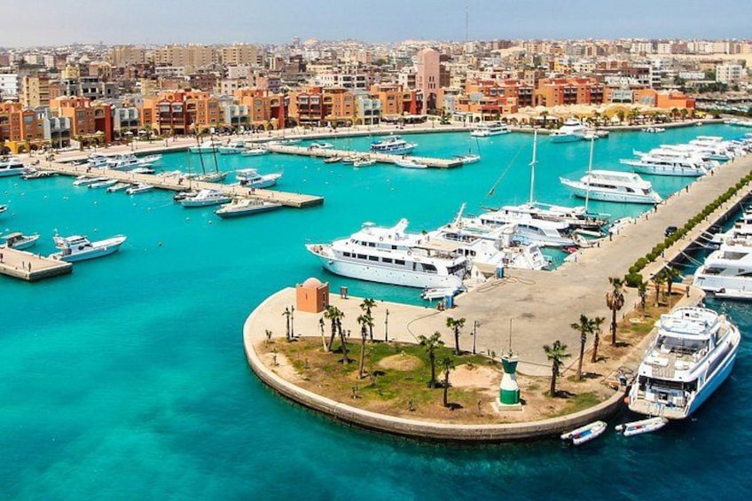 Un puerto deportivo con numerosas embarcaciones amarradas, un paseo marítimo y un paisaje urbano al fondo. 1