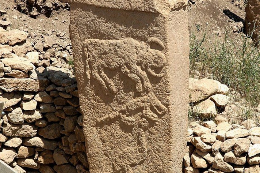 A stone pillar with carved figures and a stone wall. 4