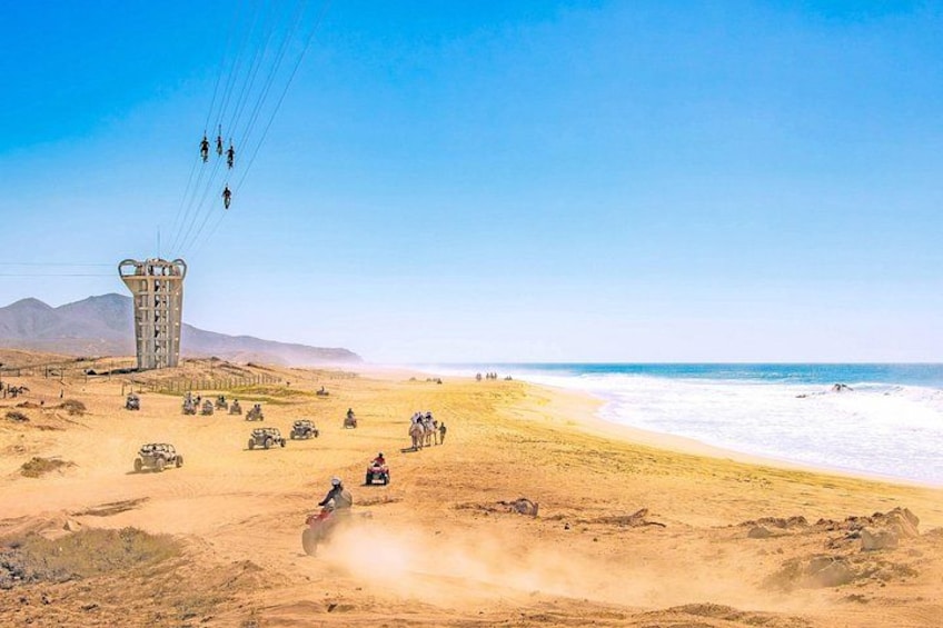 A desert landscape with a beach, a tall structure, and people riding off-road vehicles. 1