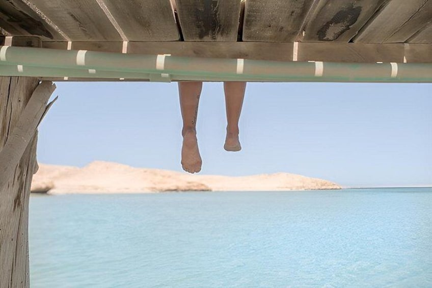 A wooden structure with a metal bar, a sandy beach, and a clear blue sea. 2