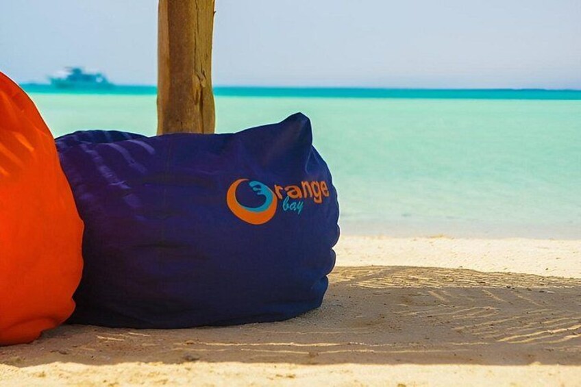 A beach with a blue bag with orange and green text, a wooden post, and a calm sea. 4