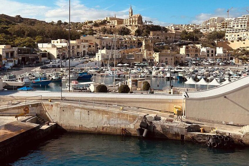 A harbor with boats, a large building, and a hill with a church. 3