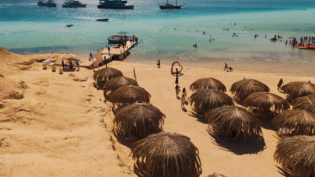 A beach with thatched umbrellas, a pier, and boats in the water. 1