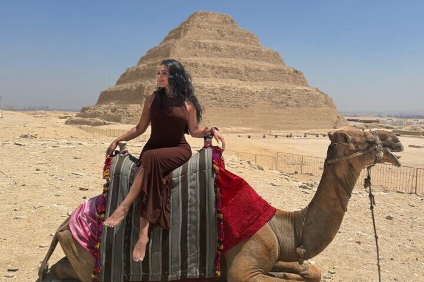A person riding a camel in a desert with pyramids in the background. 1