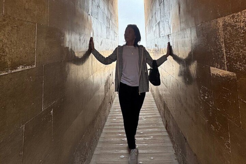 A person walking through a narrow stone corridor with their arms outstretched. 4