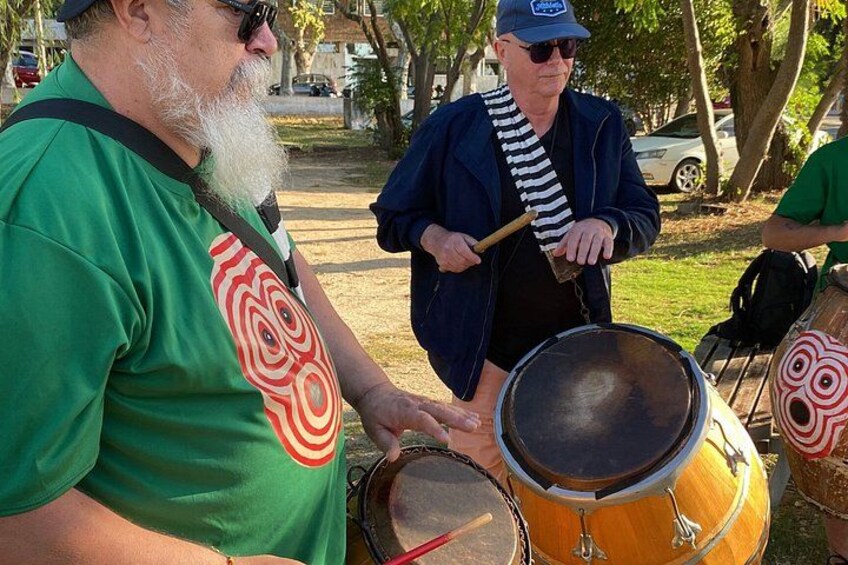 Two people playing drums in a park. 2