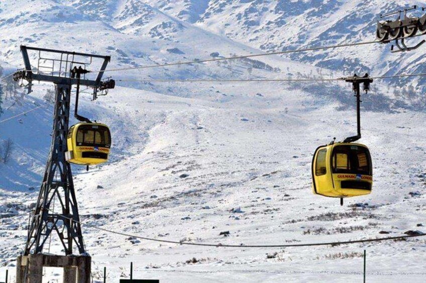 Ett snötäckt berglandskap med två gula linbanor som hänger från ett vajersystem. 4