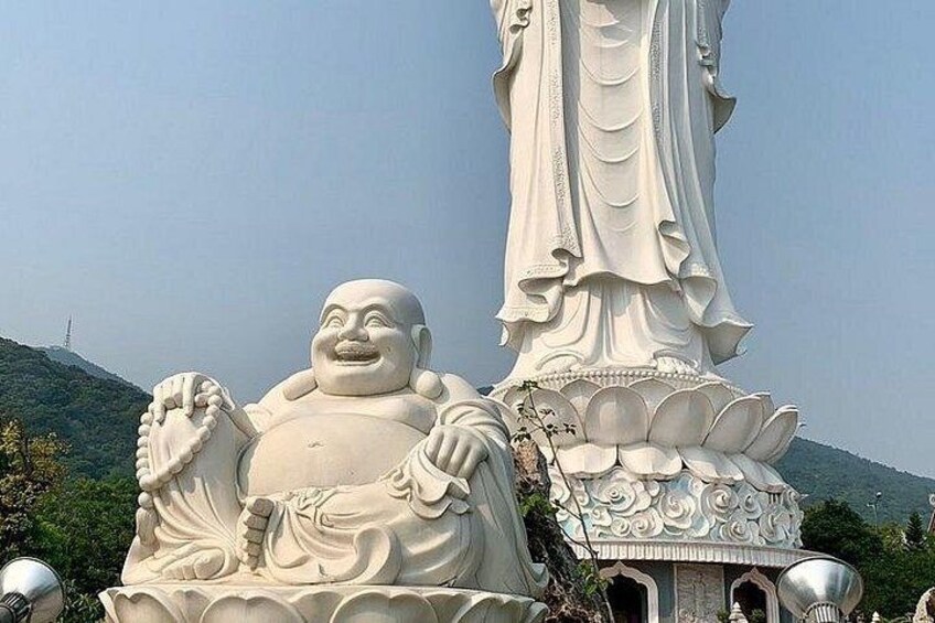 A large white Buddha statue with intricate carvings, set against a backdrop of a clear sky and a hilly landscape. 2