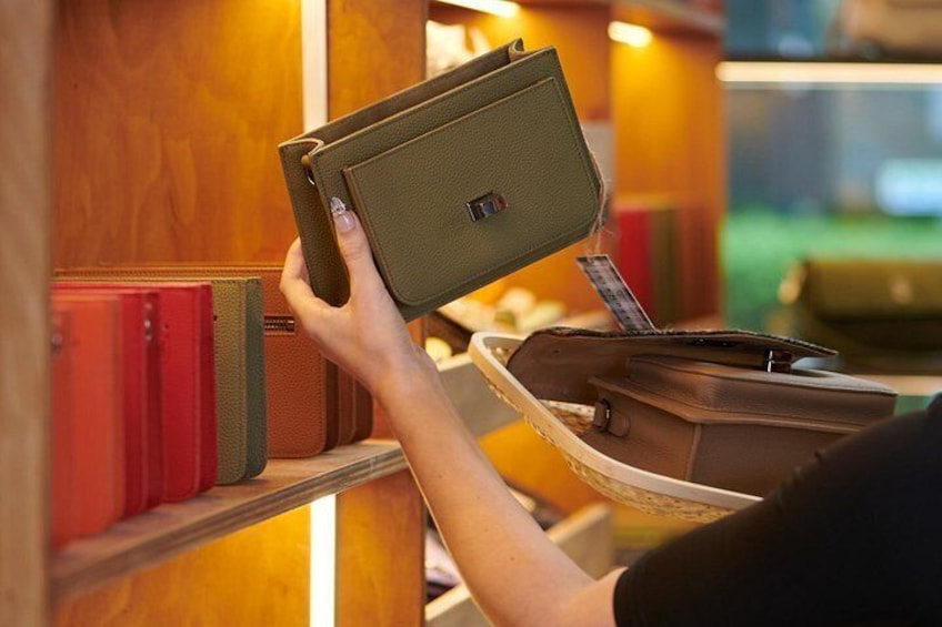 A person holding a green leather wallet with a card slot, standing in front of a wooden bookshelf with red books. 3