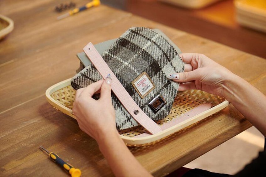 Hands assembling a woven bag with a metal clasp on a wooden table. 2
