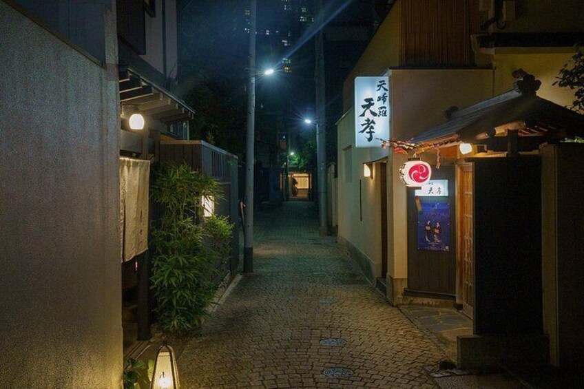 En smal gyde om natten med en restaurant til højre, et skilt med japanske tegn og en lygtepæl. 3