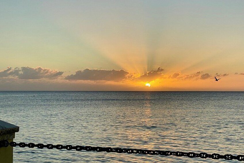 A sunset over the ocean with a chain barrier in the foreground. 3