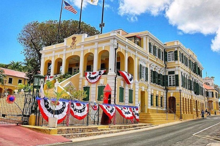 A historic building with a yellow facade, arched windows, and a flagpole with the American flag. 1