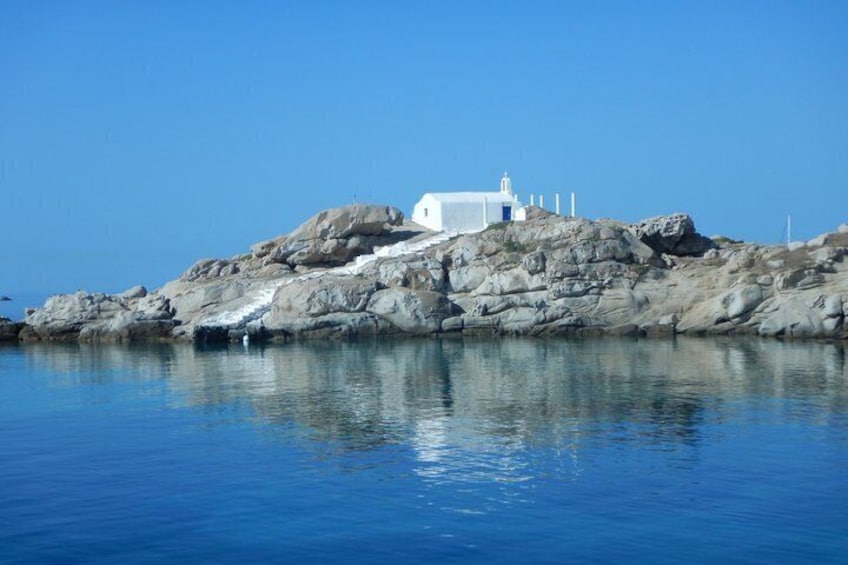 A white building on a rocky outcrop with calm blue water in the foreground. 2