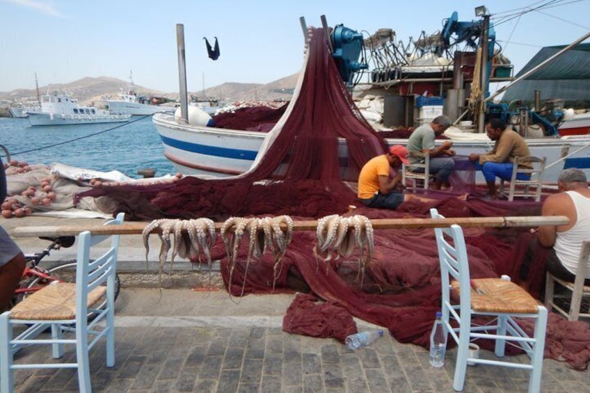 A boat docked at a harbor with fishing nets and ropes, and people sitting on chairs. 3