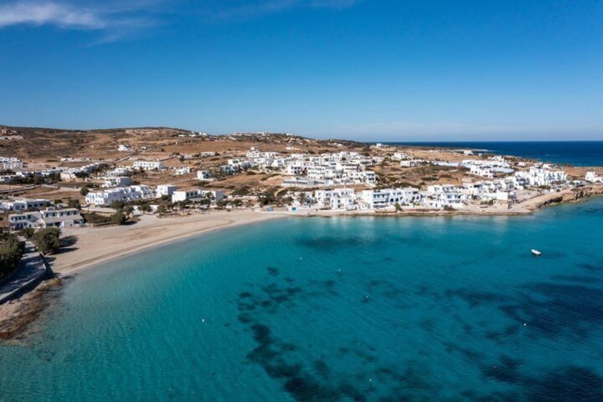 A coastal town with white buildings, a sandy beach, and clear turquoise waters. 1