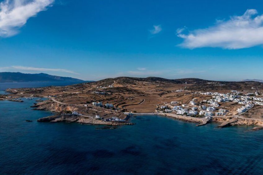 A coastal town with white buildings, a clear blue sky, and a hilly landscape in the background. 4