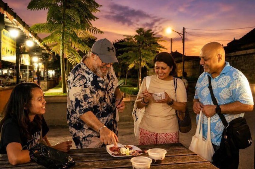 A group of people dining outdoors at dusk with a sunset in the background. 1