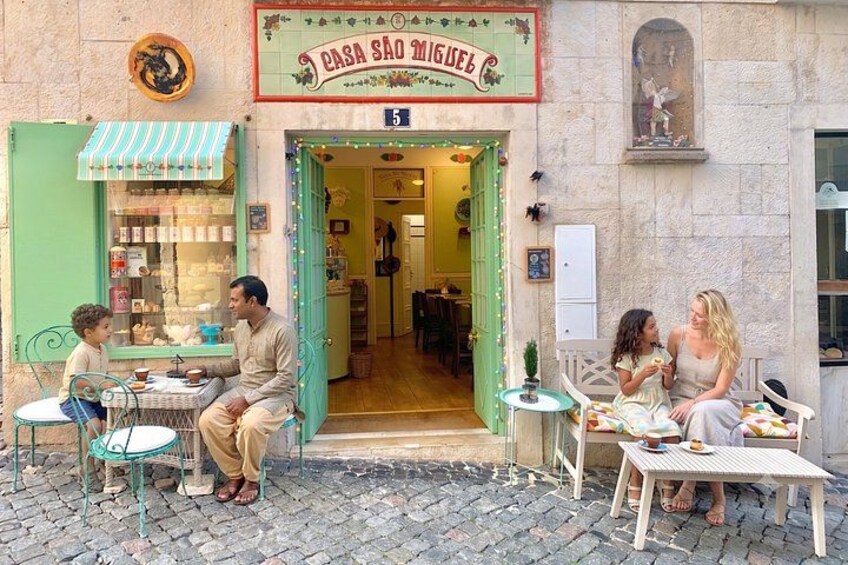Une scène de rue avec un café appelé « Casa São Miguel » et des personnes assises à des tables en terrasse. 1