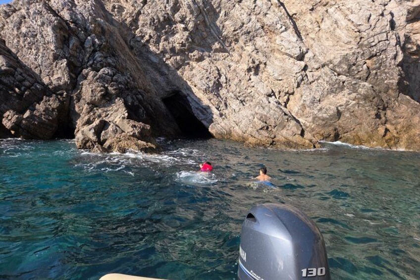 Una costa rocosa con agua azul cristalina, una persona nadando y un bote con motor. 5