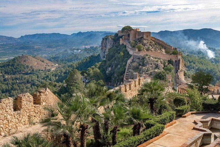 A historic fortification on a hilltop with surrounding greenery and a distant view of the landscape. 1
