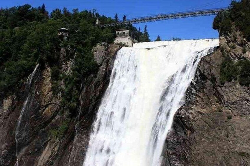 A large waterfall cascading down a rocky cliff, a bridge in the background, and a small building on the cliff. 2