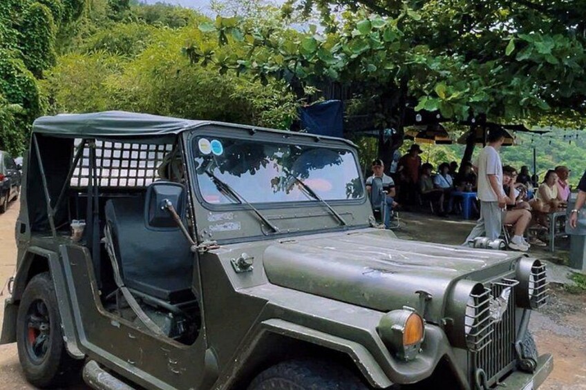 A military-style jeep parked outdoors with people in the background. 1