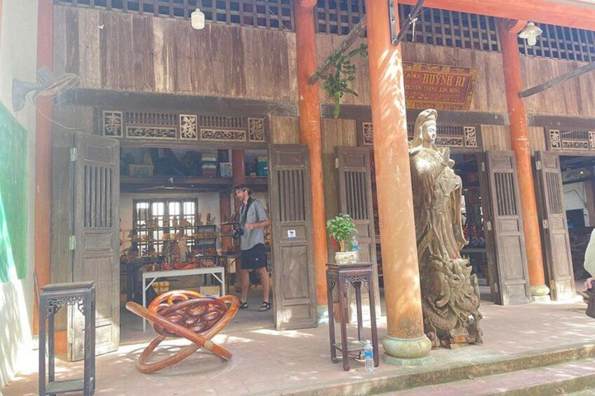 A traditional wooden building with a statue, a person standing near the entrance, and a wooden chair in the foreground. 3