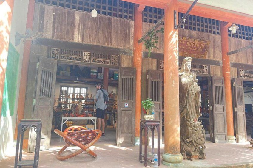 A traditional wooden structure with a statue, a person standing at the entrance, and a display of goods. 5