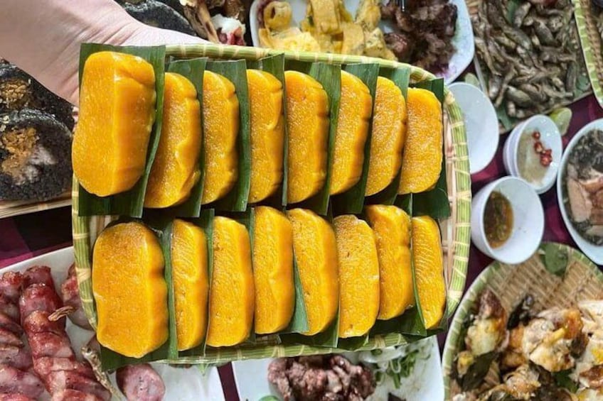 Ett fat med skivor av gul mango, placerat på ett grönt blad, omgivet av olika rätter. 4