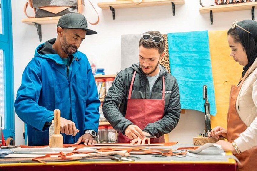 Tre personer arbejder ved et bord med værktøj og materialer, måske i et værksted eller et kreativt atelier. 5