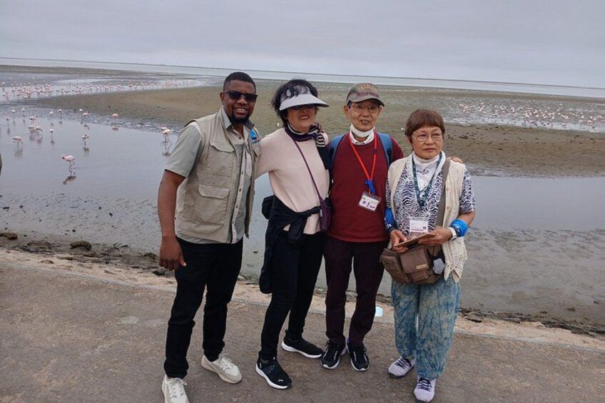 A group of people standing on a beach with flamingos in the background. 2