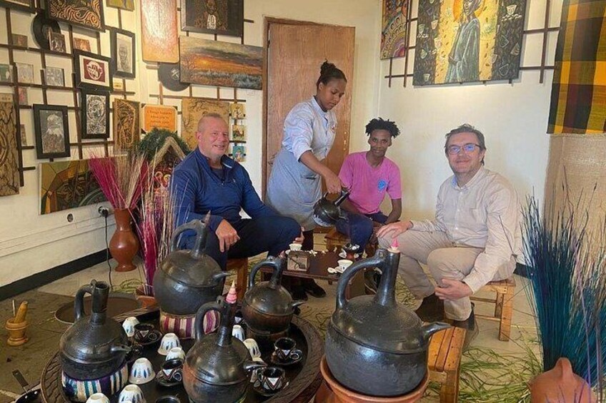 Een groep mensen in een kamer met traditioneel aardewerk en kunstwerken aan de wanden. 1