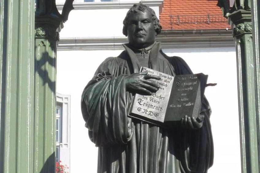 Une statue représentant un homme tenant un livre, avec un bâtiment en arrière-plan. 2