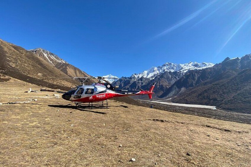 A red and white helicopter parked on a grassy field with a mountainous backdrop. 2