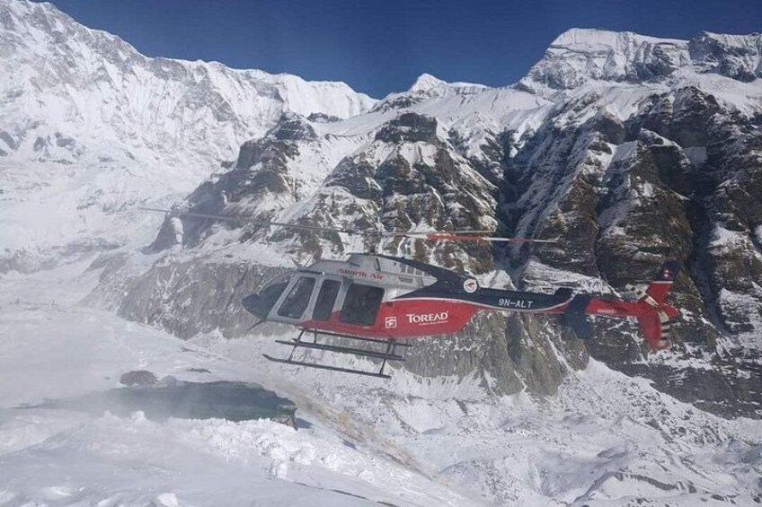 A red and white helicopter with 'Toread' and '9-N-ALT' on its side, flying over a snowy mountainous terrain. 5