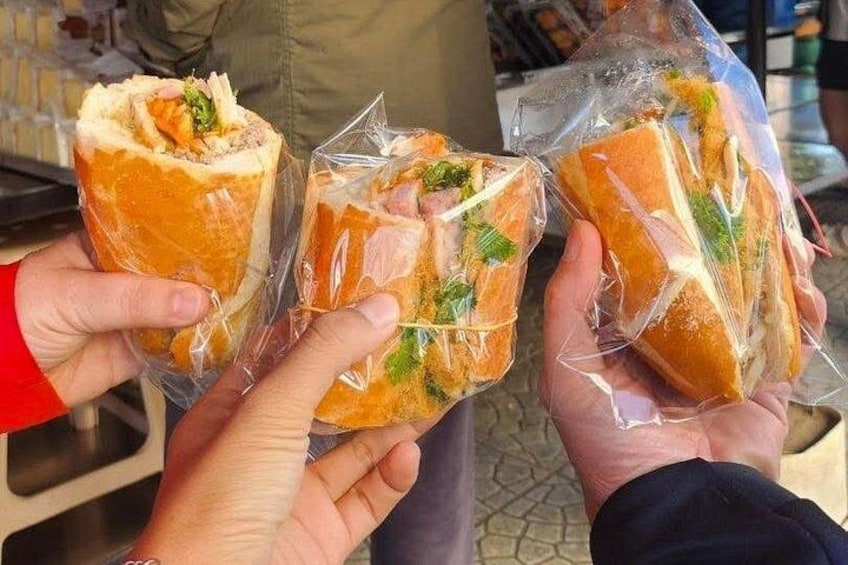 Three people holding sandwiches wrapped in plastic. 4