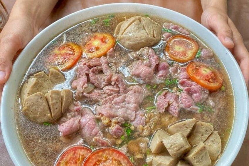 A bowl of soup with meat and tomato slices. 5