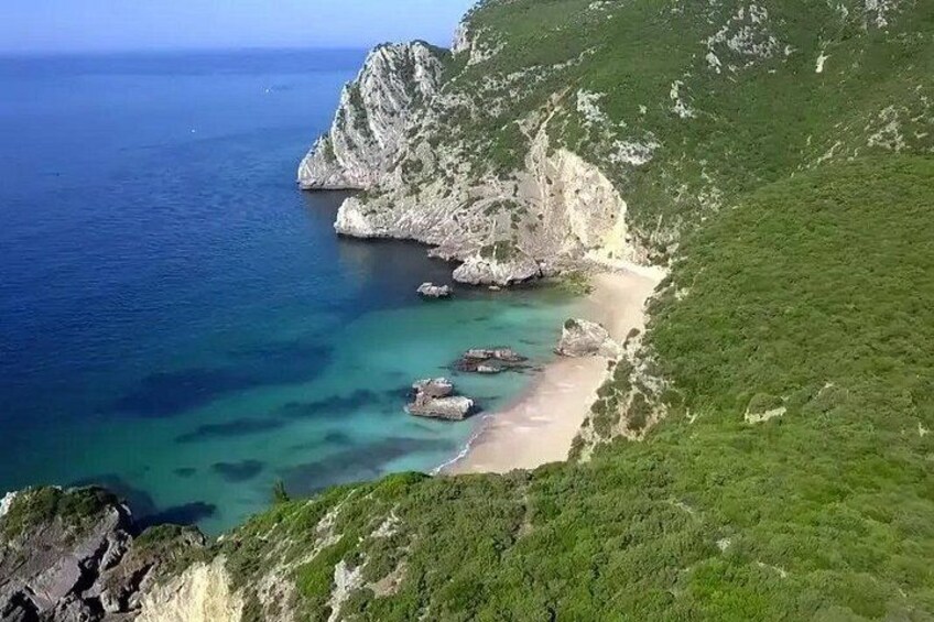Eine Küstenlandschaft mit steilem Felsen, einem Sandstrand und klarem, blauem Wasser. 3