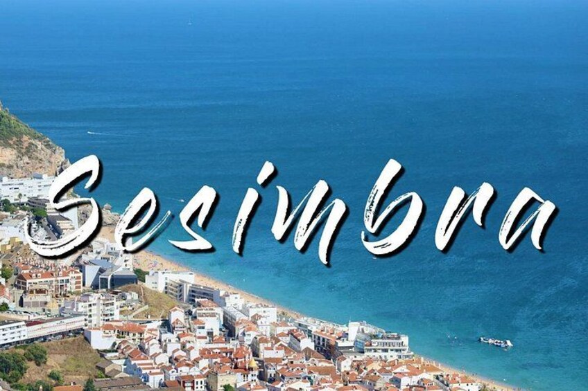 Eine Küstenstadt mit der Aufschrift 'Sesimbra', mit Strand, Gebäuden und blauem Meer. 4