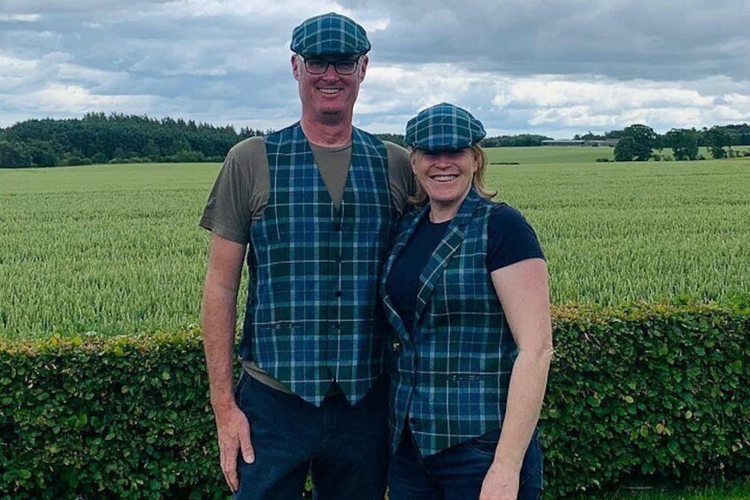 Two people standing in a field with a hedge in the foreground and a cloudy sky in the background. 1