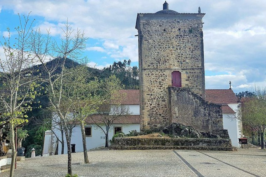 A stone tower with a red door, surrounded by white buildings with red roofs, set against a backdrop of hills and trees. 2