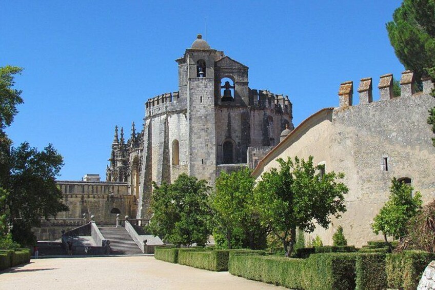 A historic stone building with a bell tower, surrounded by well-maintained hedges and a clear sky. 5