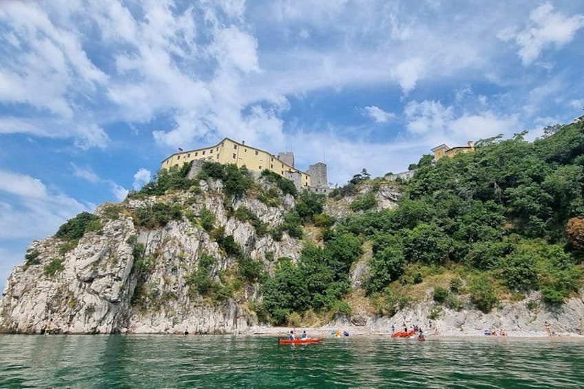 A coastal landscape with a historic building on a cliff, clear blue sky, and calm sea. 4