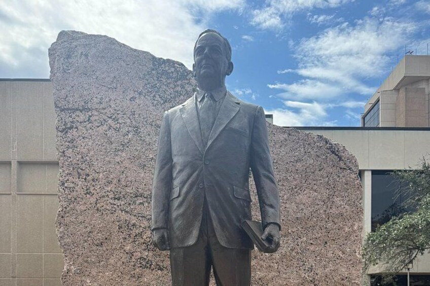A statue of a man in a suit holding a book, standing in front of a large rock formation. 5