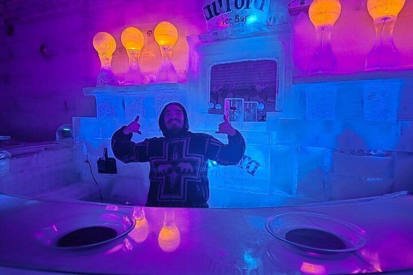 A person in a cross-stitched sweater in front of an ice bar with illuminated ice sculptures. 3
